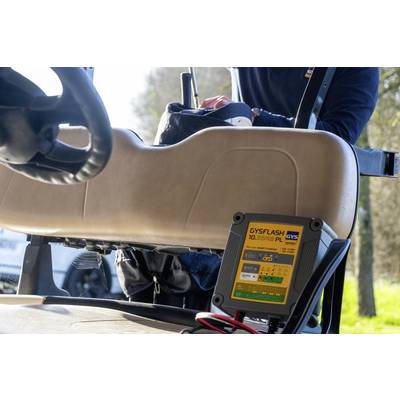 A person is charging a golf cart with a GYSFLASH 10.36 PL battery charger. The device is mounted on the back seat of the vehicle.