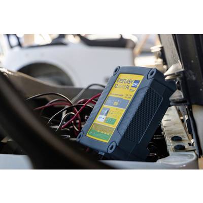 A battery charger is connected to a vehicle battery. The device displays operational information on a yellow screen.