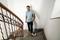 A man is standing barefoot on a staircase, holding a vacuum cleaner. He is smiling and appears to be cleaning.