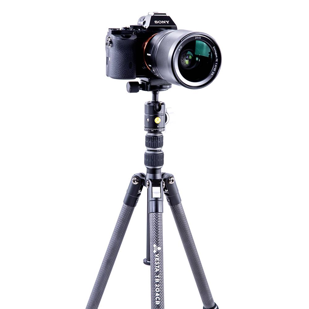 A black camera with a lens sits on a professional tripod against a white background.