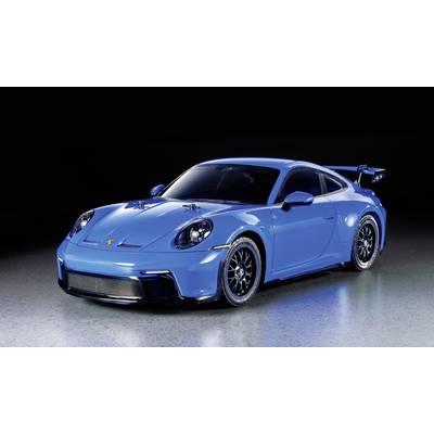 A blue sports car with a black spoiler and wheels stands on a reflective surface, illuminated from above.
