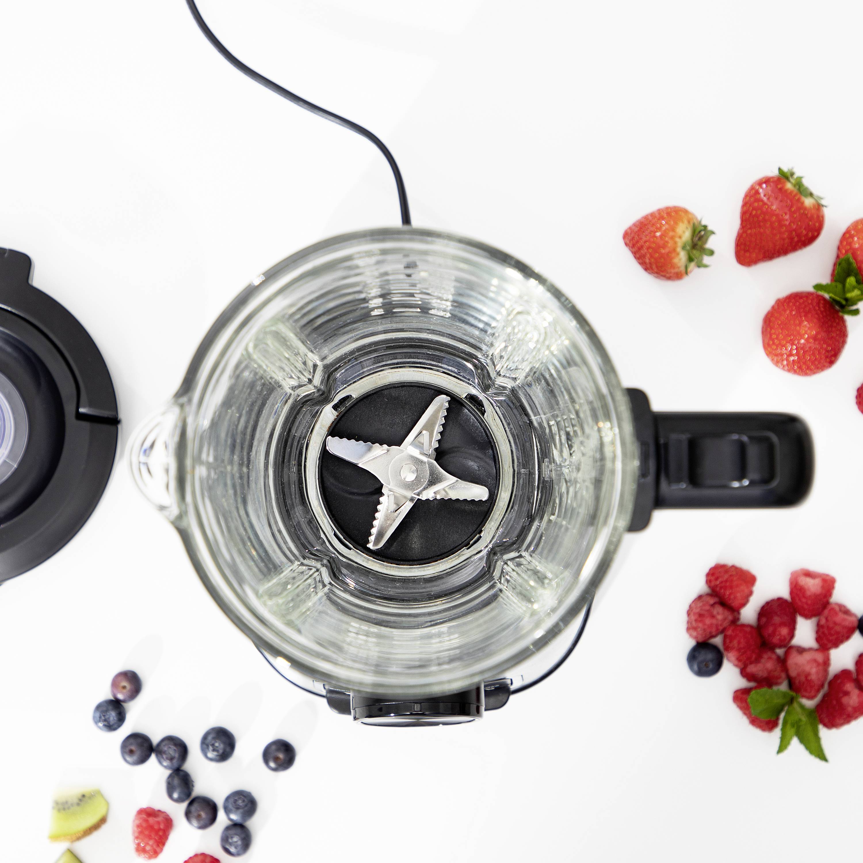 A blender with its lid open, surrounded by strawberries, raspberries, and blueberries on a white table, viewed from above.