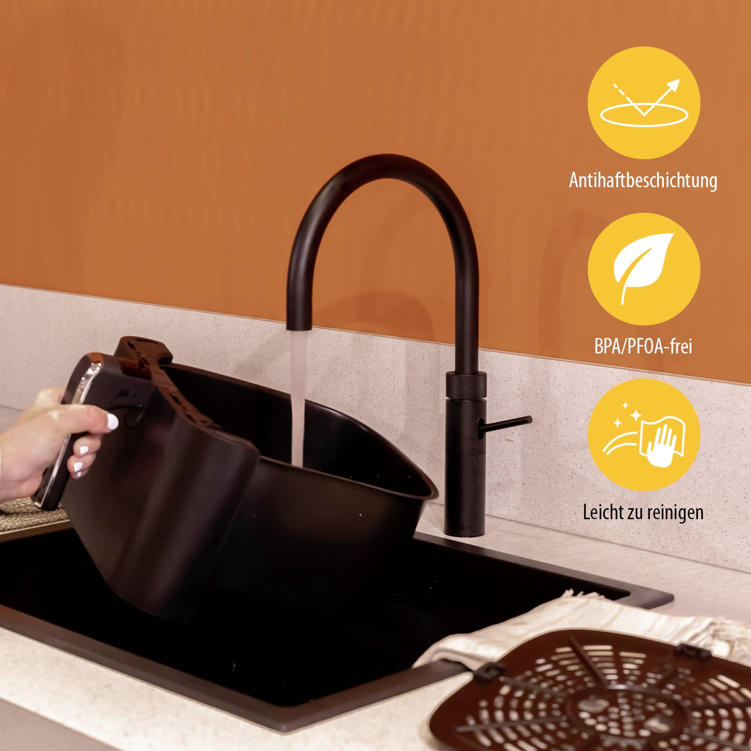 A person is rinsing a black deep-fryer basket under a black tap. Symbols indicate 'non-stick coating', 'BPA/PFOA-free', 'Easy to clean'.