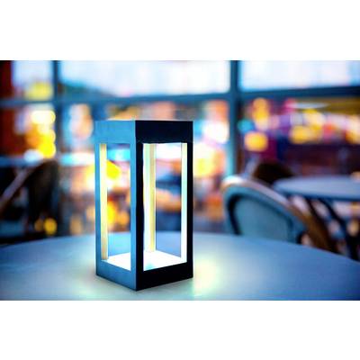 A modern, luminous table lamp sits on a table in a softly, atmospherically lit café or restaurant.