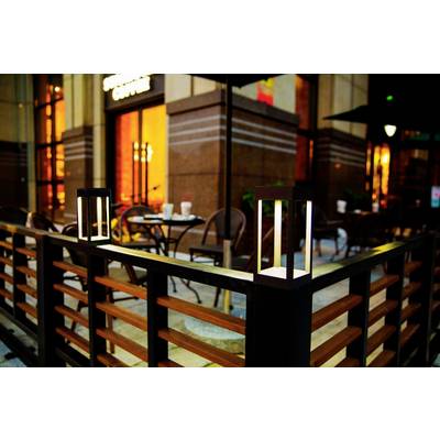 An exterior view of a cosy café with a table and chairs, surrounded by a decorative fence with two glowing lanterns.