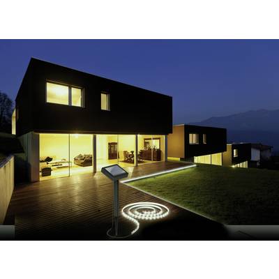 A modern, square house with large, illuminated windows at night, surrounded by a well-maintained garden with a lit pathway.