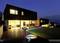 Two modern, minimalist houses at dusk. The garden is adorned with colourful LED lights illuminating a pathway.