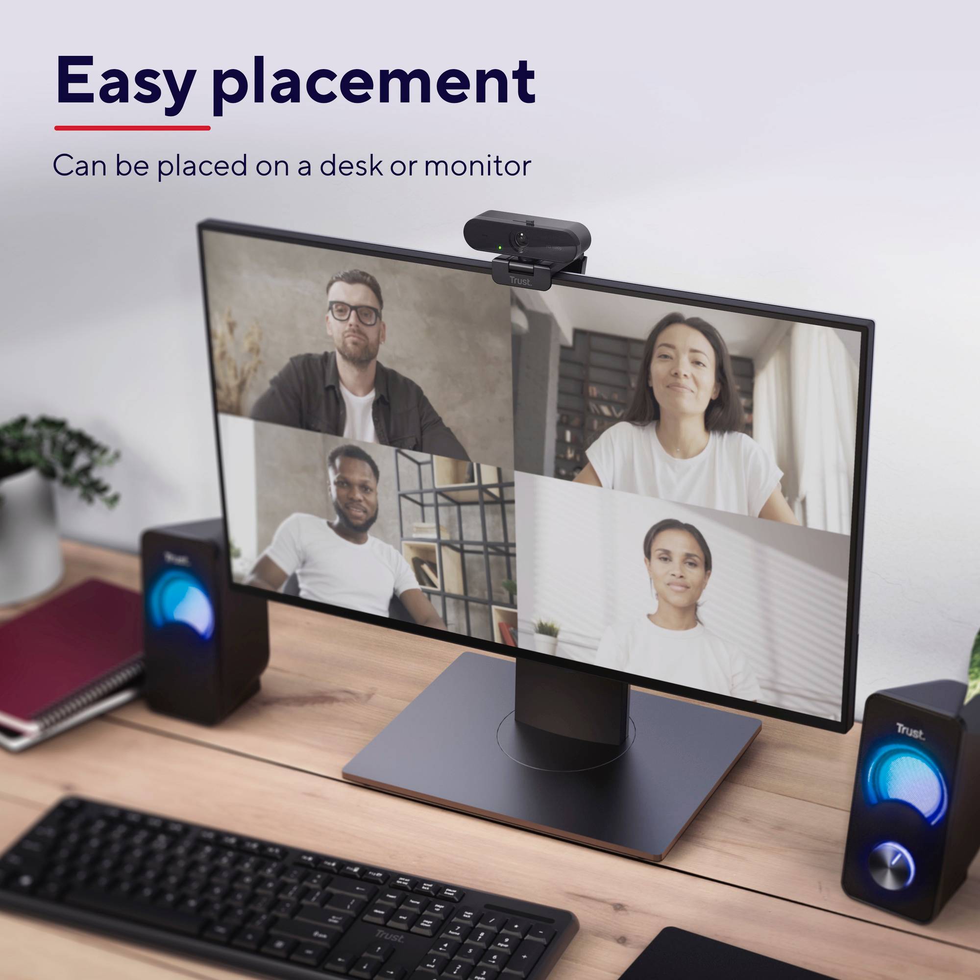 Video conference on a monitor, showing a virtual meeting with four people. The monitor is placed on a desk.