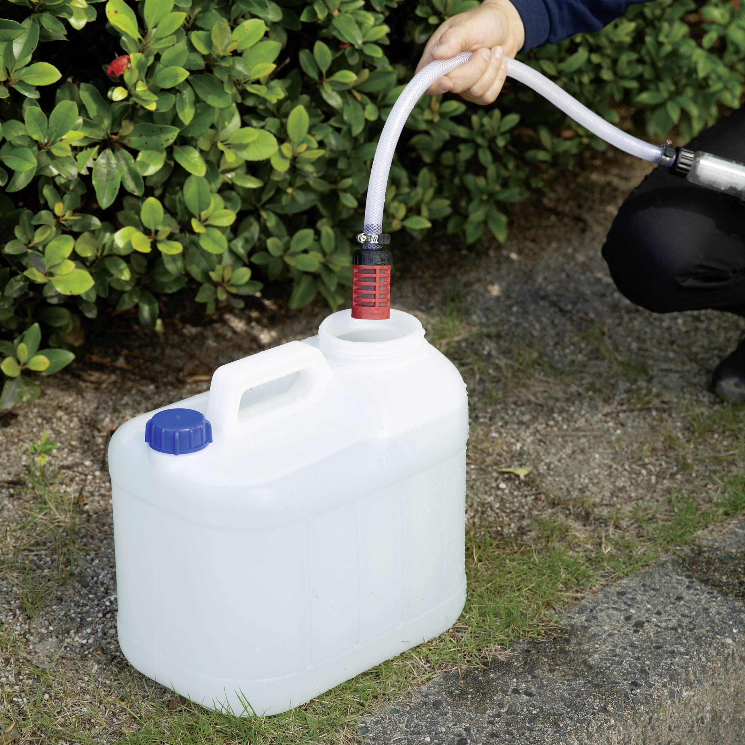 A person is filling a white container with liquid using a hose. Plants are visible in the background.