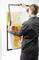A person is hanging a piece of artwork with a yellow and orange motif on the wall.