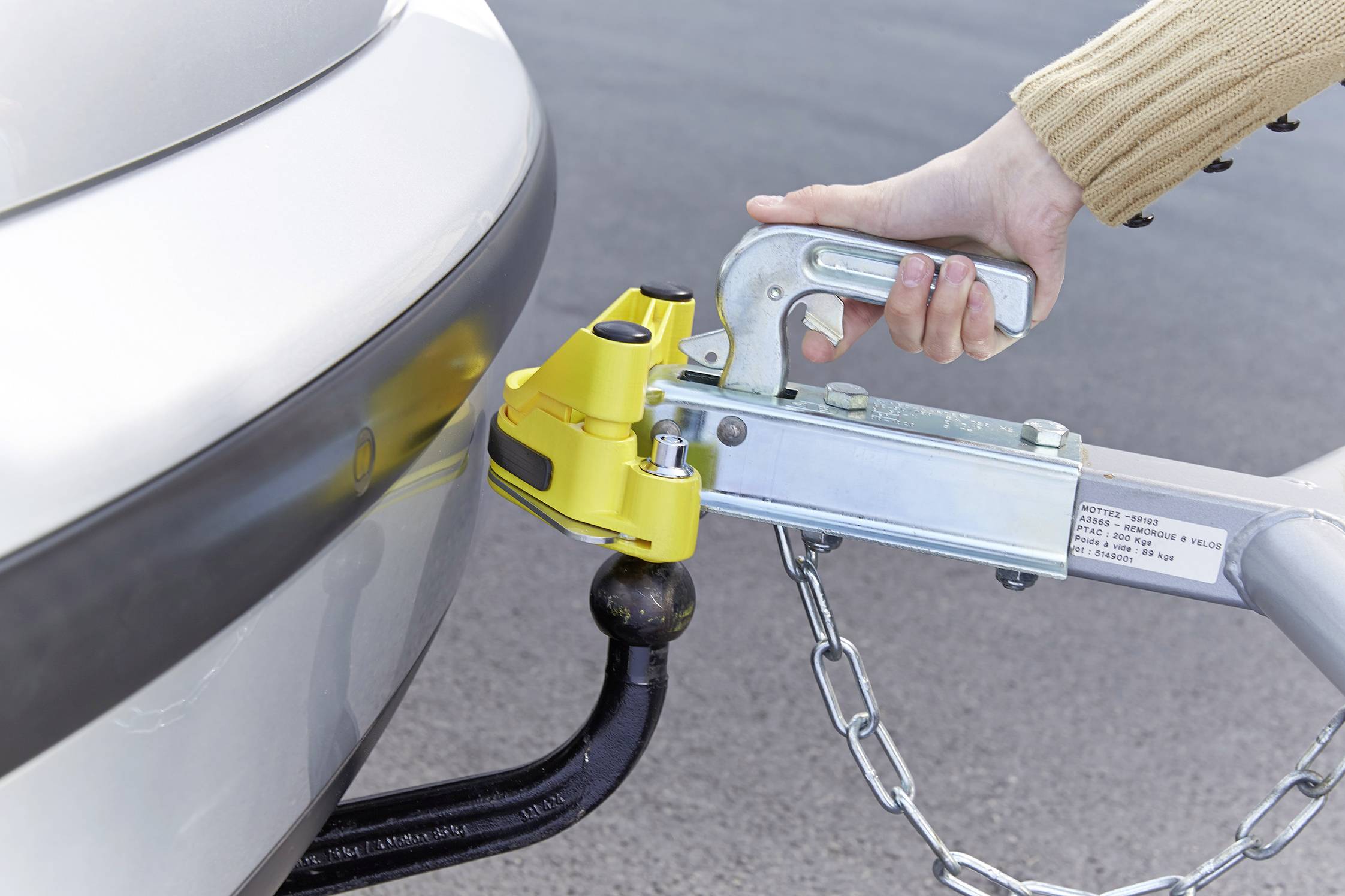 A hand is securing a yellow tow bar to a tow ball at the rear of a car.