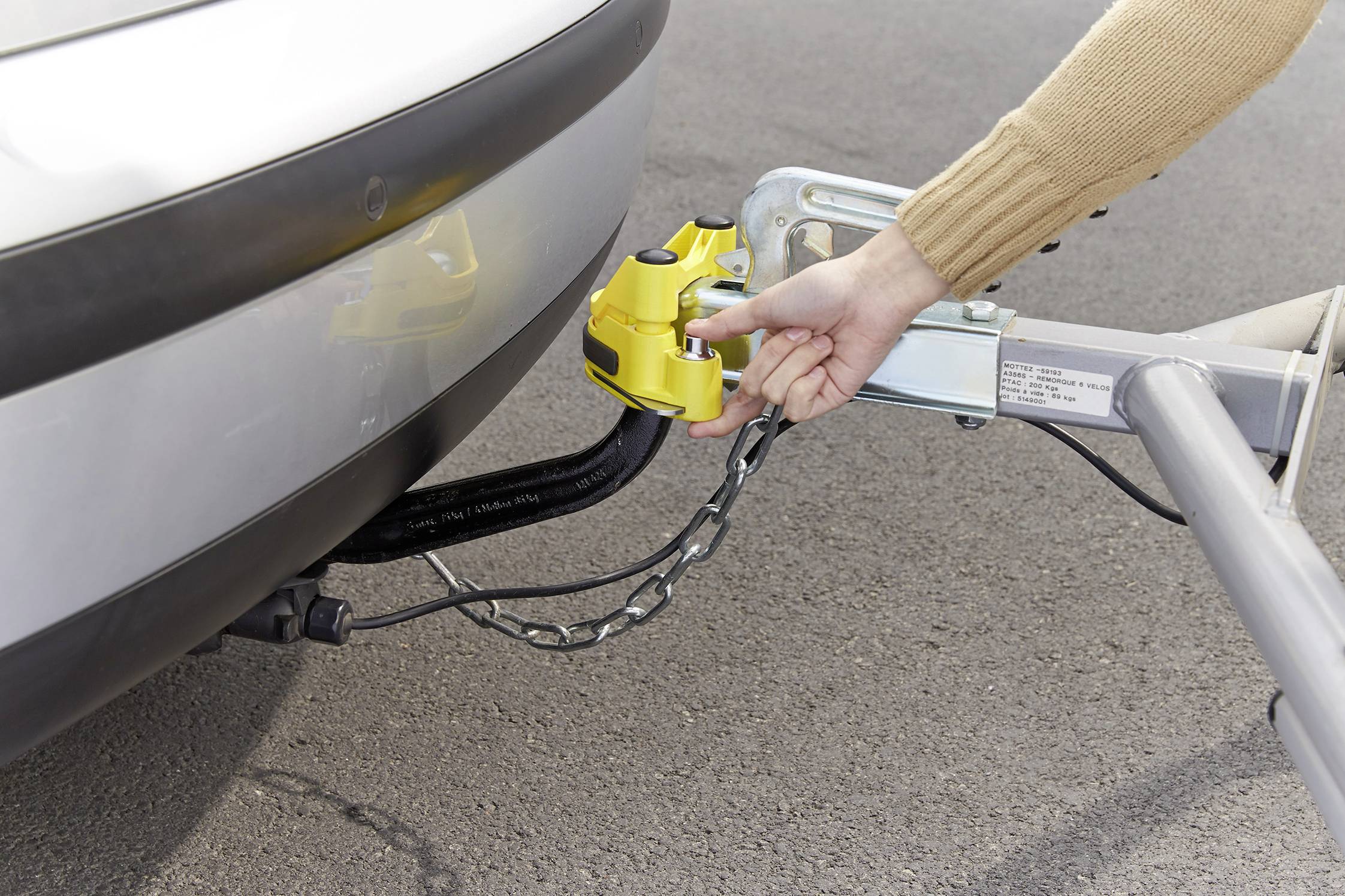 A person is attaching a yellow tow bar to a vehicle. The coupling connects the trailer to the car for safe transportation.