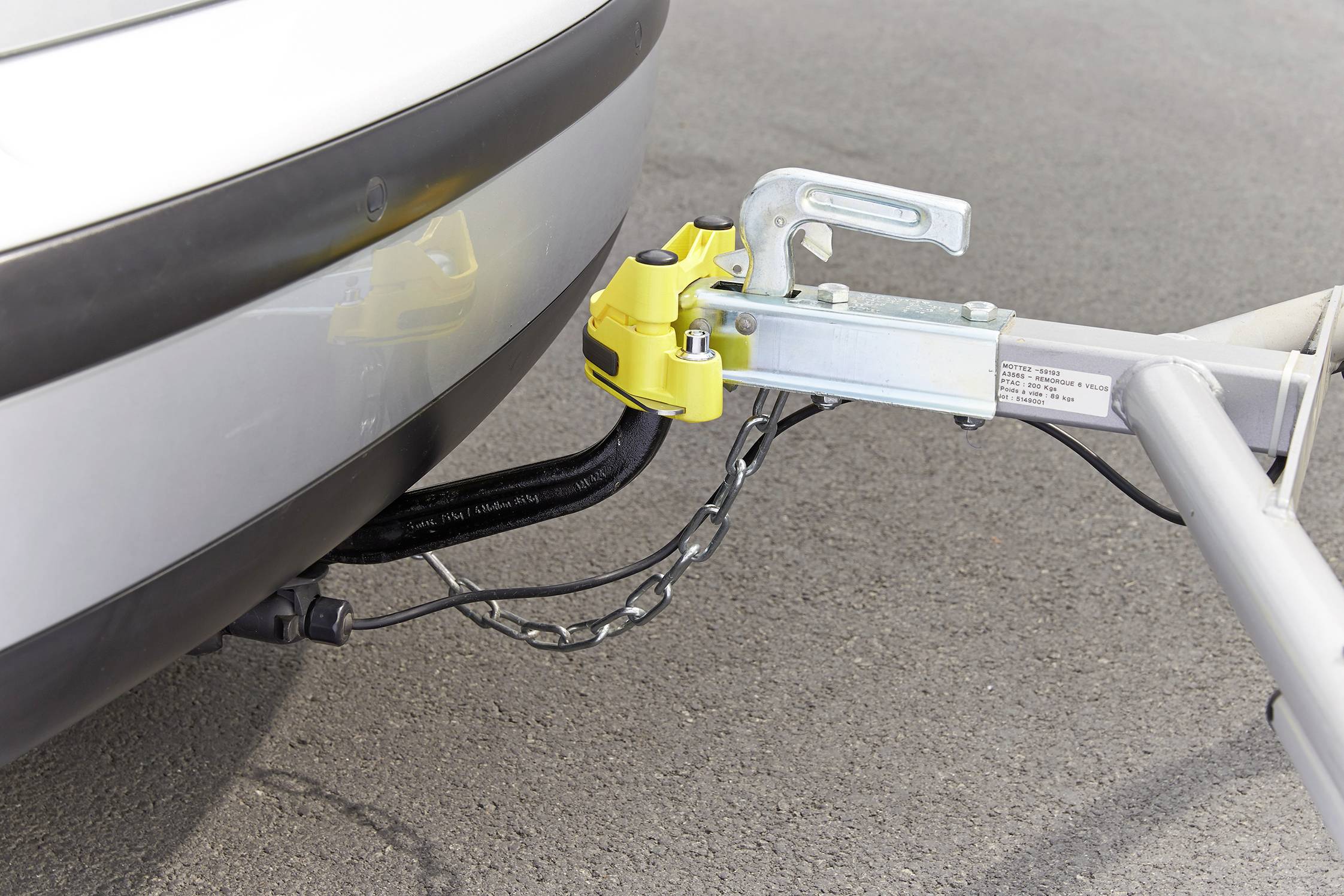 A tow bar connects a car with a trailer. A yellow safety lock prevents the trailer from becoming detached.