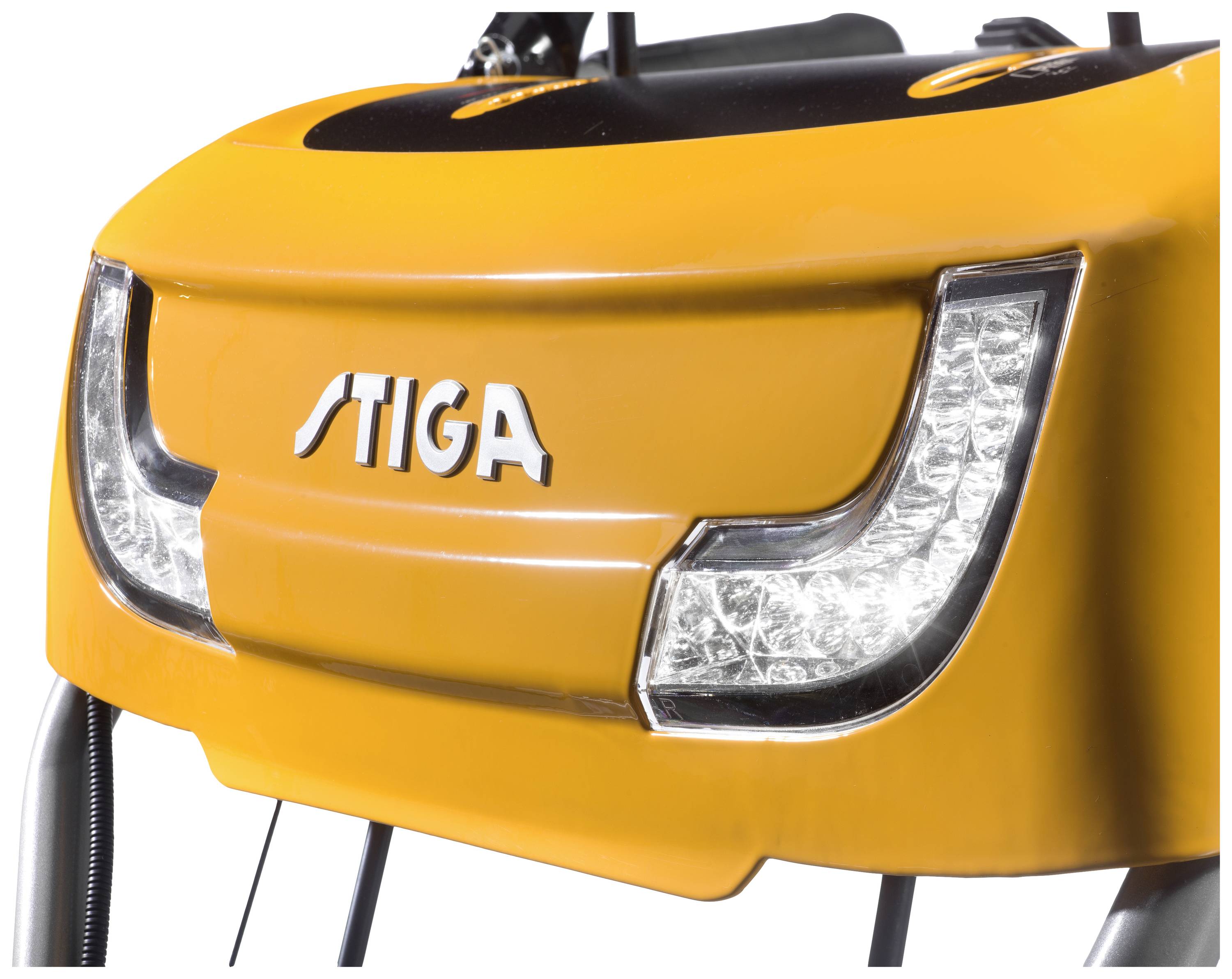Lawn mower close-up shows the front view with the brand name. Two lights are visible. The machine is yellow in colour.