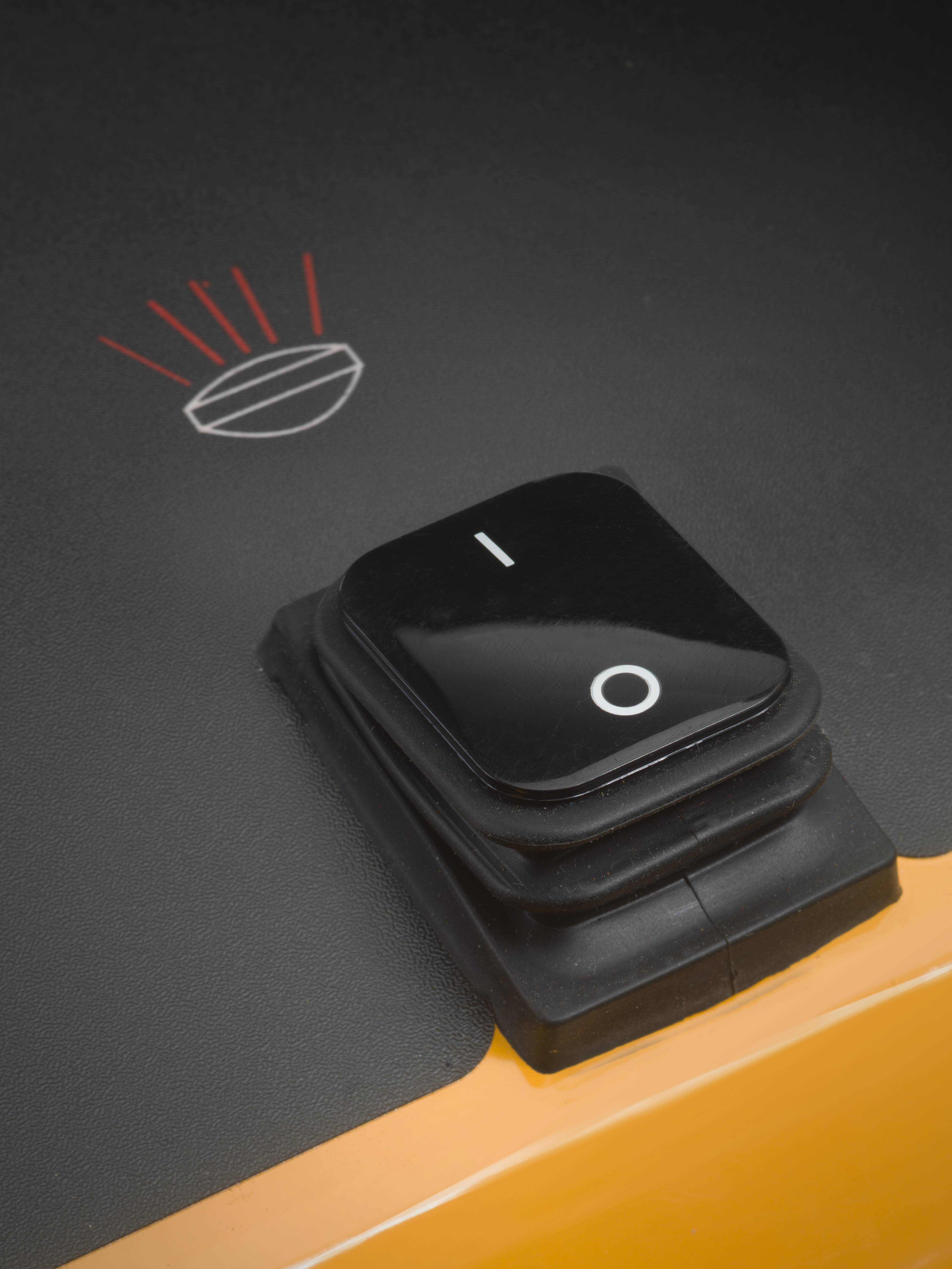 A black rocker switch with the symbols 'I' and 'O' is situated on a yellow surface. It is switched to the 'I' position.