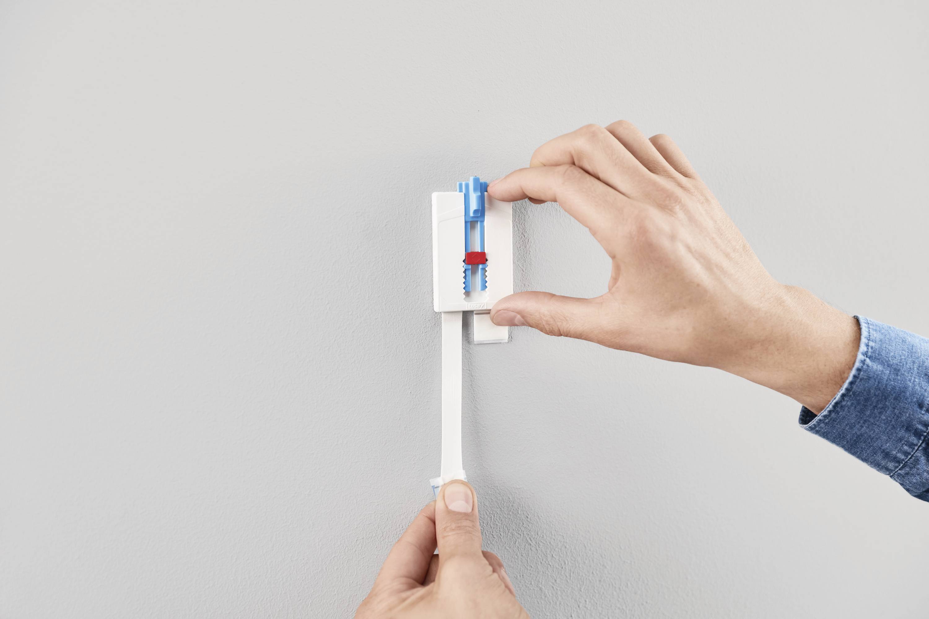 A person is installing a wall plug using a mounting tool on a wall.
