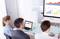 Three people in a meeting room are examining a presentation with diagrams and charts on a screen.