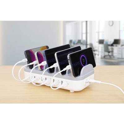 Several smartphones are being charged simultaneously at a charging station. A blurred office can be seen in the background.