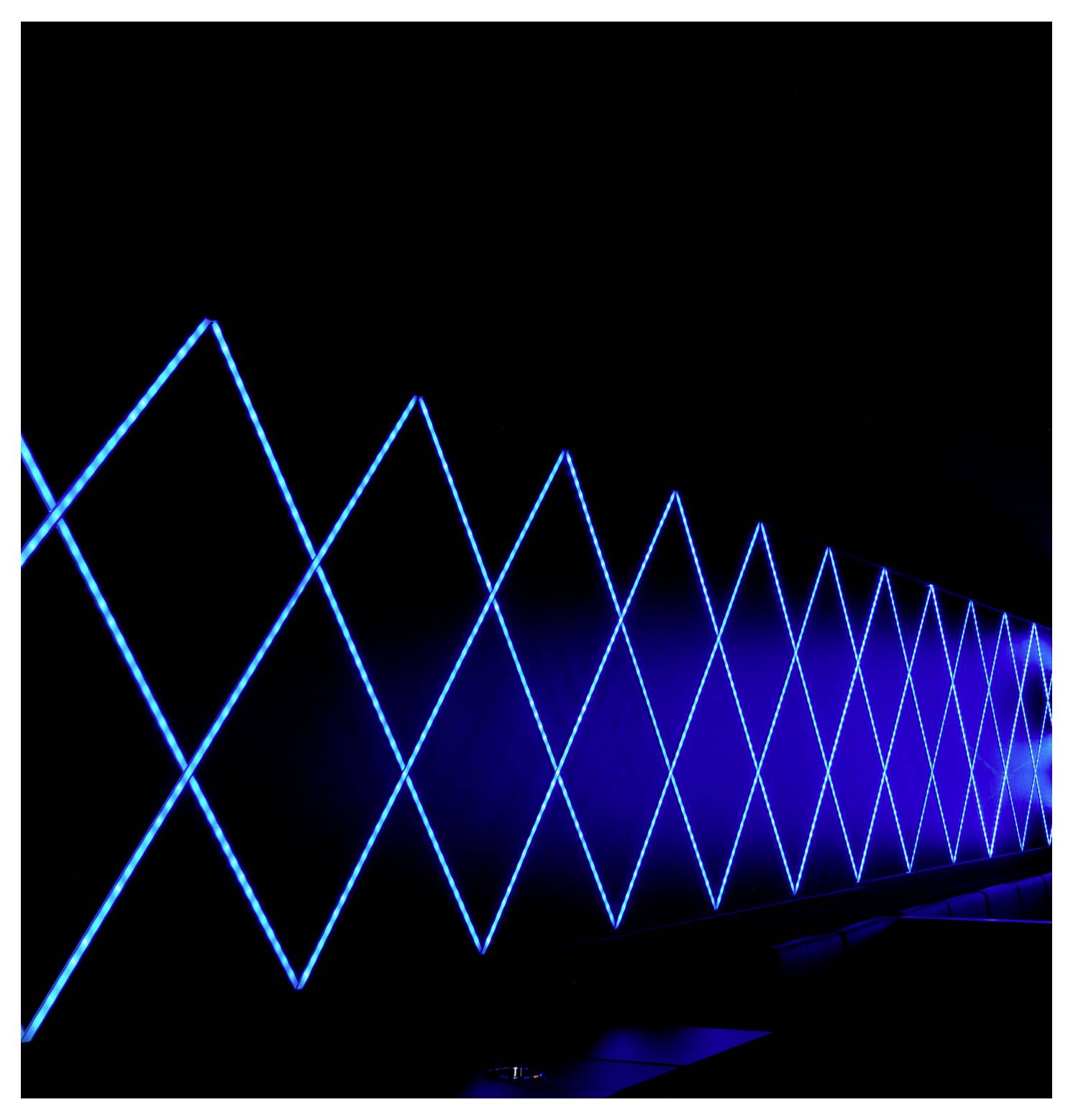 Blue neon zigzag light installation receding into the distance against a black background, creating a tunnel-like perspective.<br>