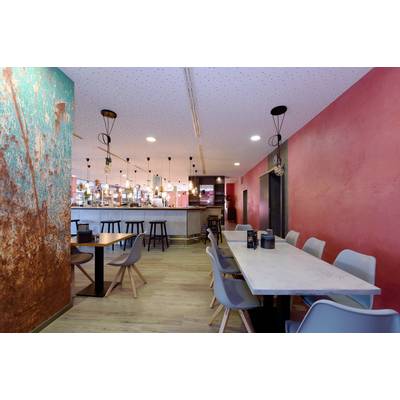 A modern café with colourful walls, a long bar, seating areas with grey chairs, stylish lighting, and a wooden floor.
