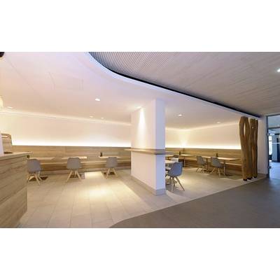 A modern, minimalist-designed café area with wooden tables and grey chairs, surrounded by warm indirect lighting.