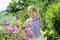 A person is spraying pink blossoms with a spray bottle in the garden. Green plants are visible in the background.
