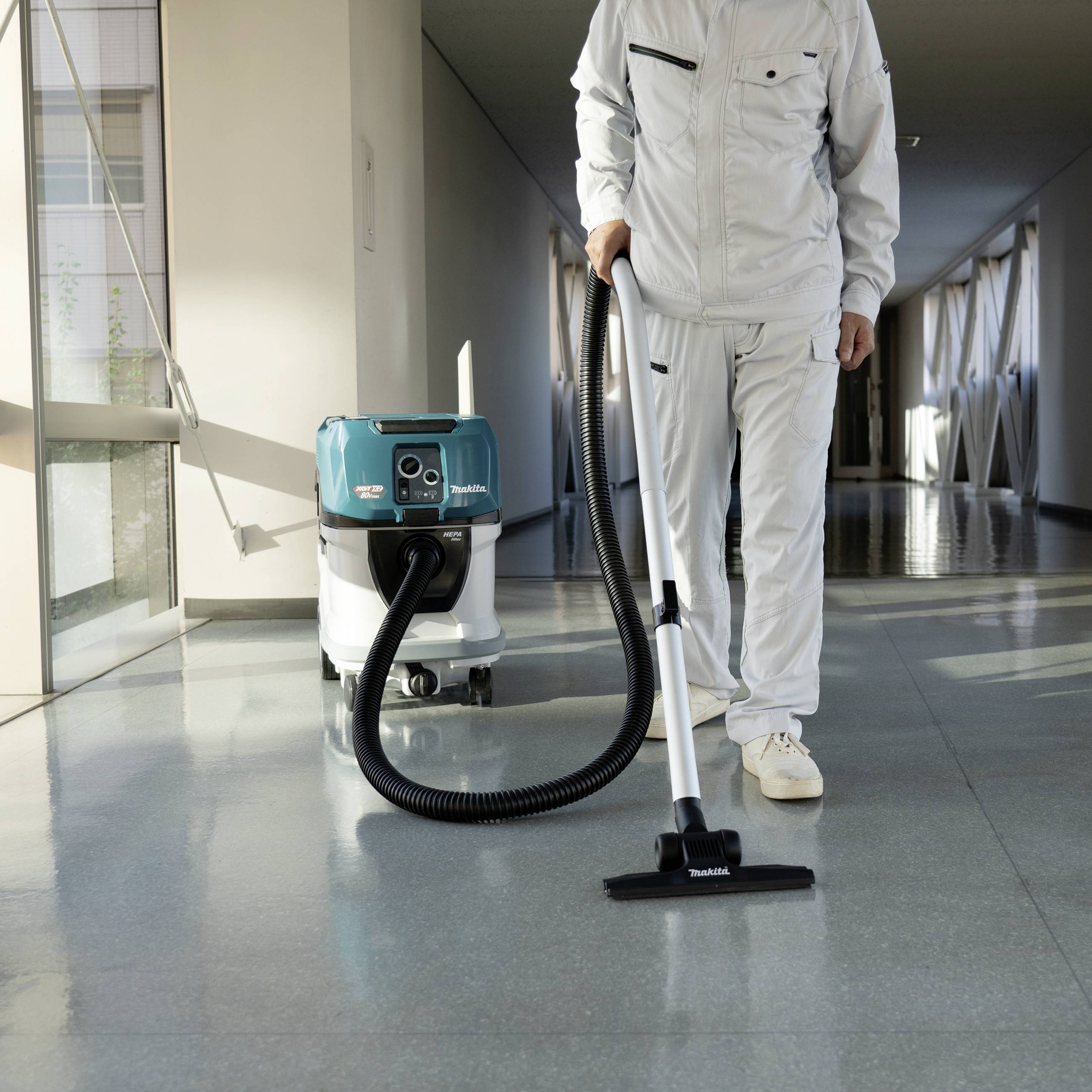 A person in work attire is vacuuming the corridor of an office building with a professional hoover.