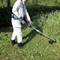 A person in protective clothing is using a strimmer to cut grass and weeds in a garden. Bushes and meadows can be seen in the background.