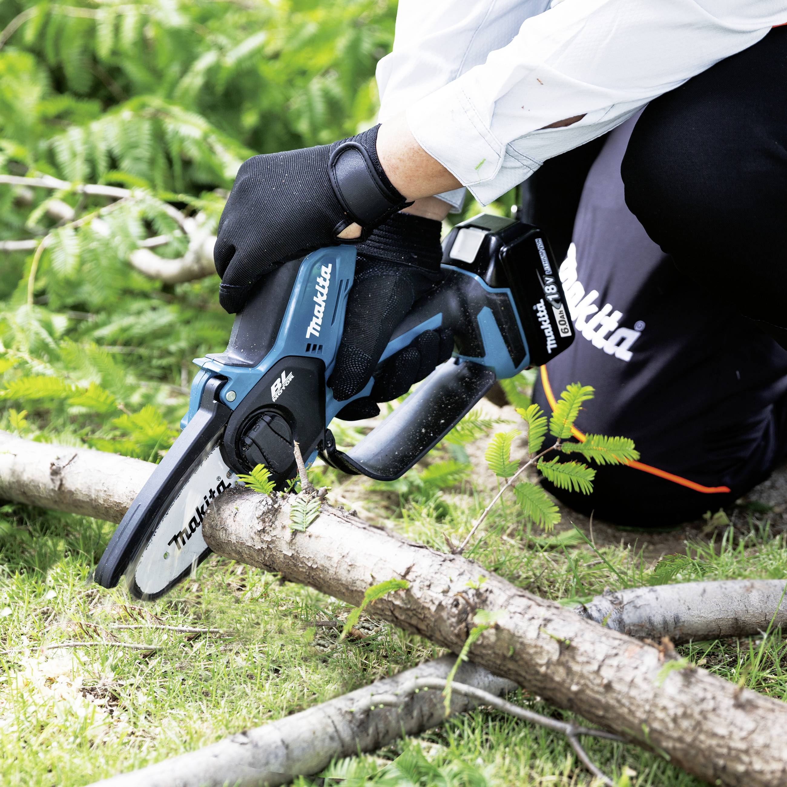 A person is cutting a branch with a cordless saw on a lawn. They are wearing gloves and a Makita logo is visible.