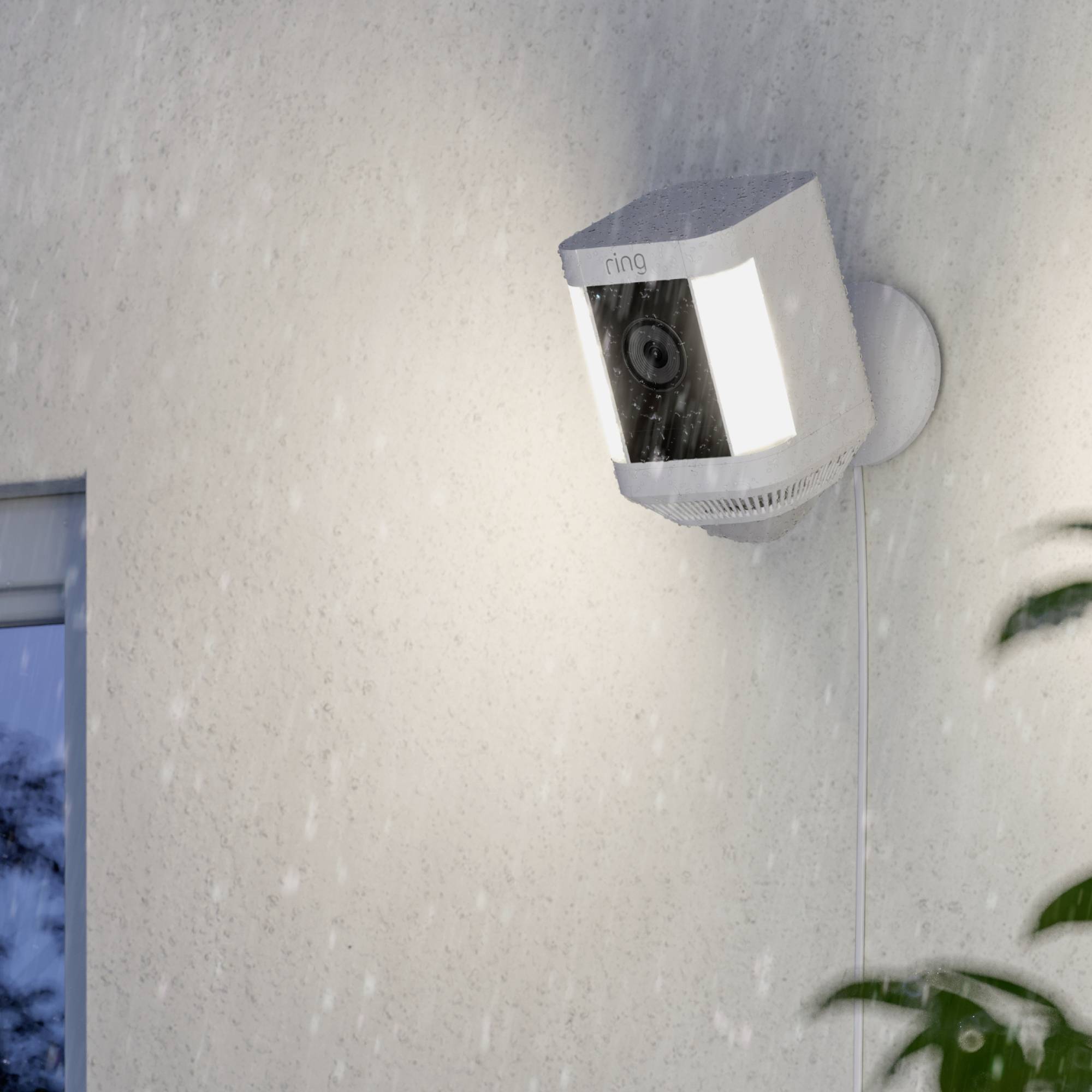 Security camera on a house wall during rain, illuminating the area.