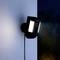 A security camera with lighting is mounted on a wall and filming outside at dusk.