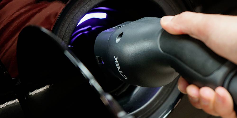 Electric car being charged at a charging point, hand holding charging cable at the connection.