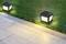 Two solar-powered lamps illuminate a garden path. The lamps are cuboid in shape and stand on a lawn area beside the path.