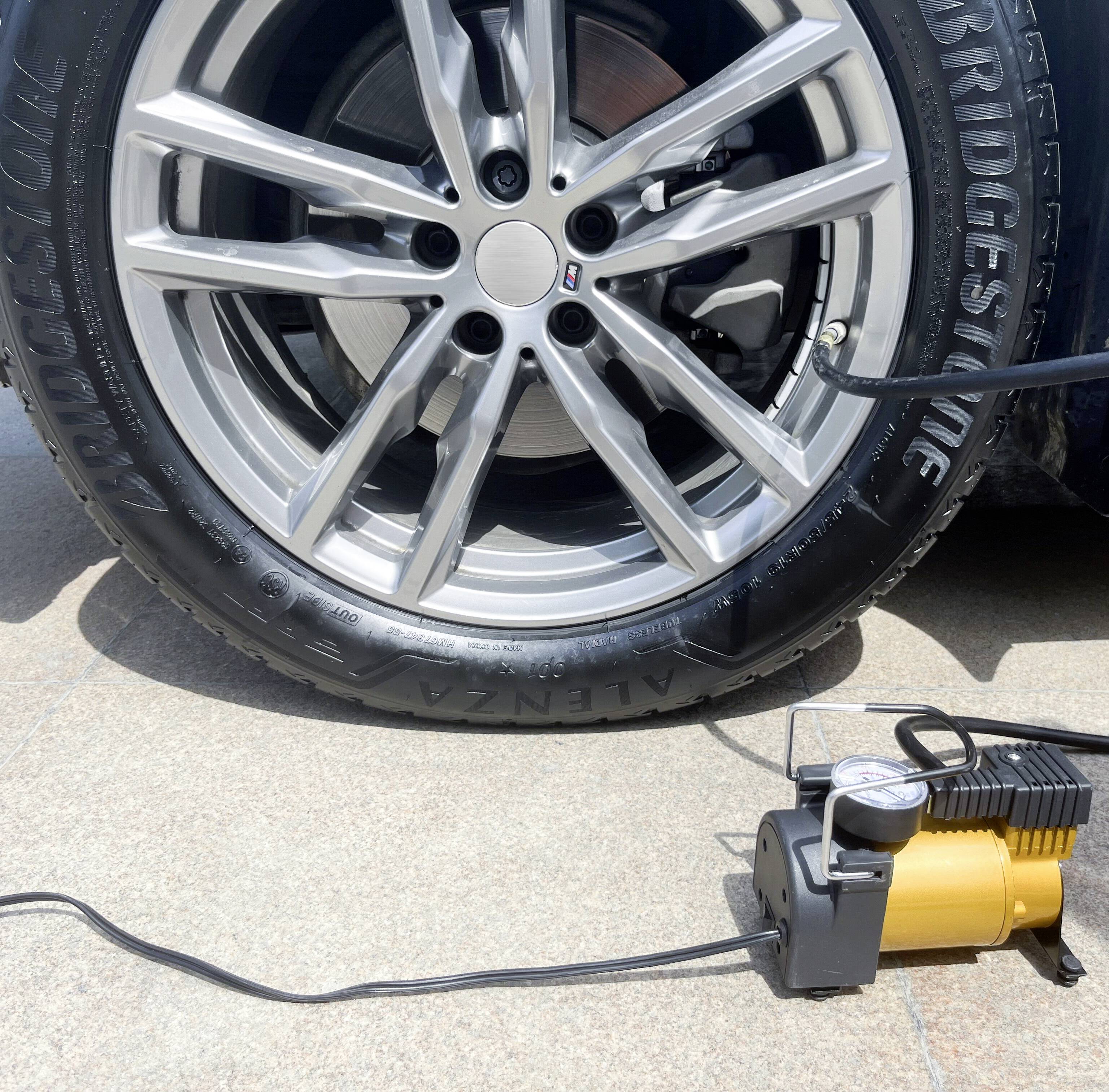 A tyre of a car is being inflated with a portable compressor. The compressor is yellow and black and is lying on the ground.