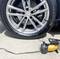 A tyre of a car is being inflated with a portable compressor. The compressor is yellow and black and is lying on the ground.
