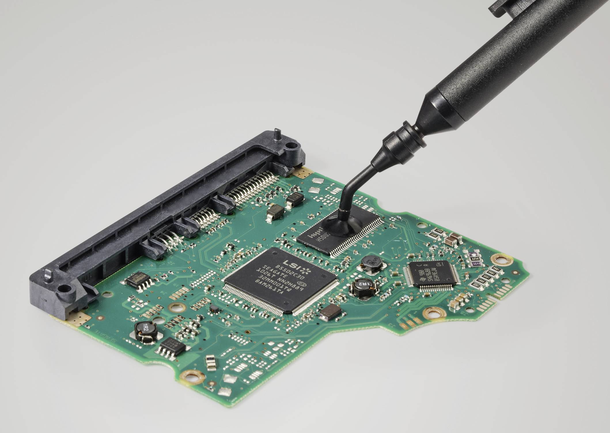 A green circuit board with electronic components and a black tool placed on its surface.