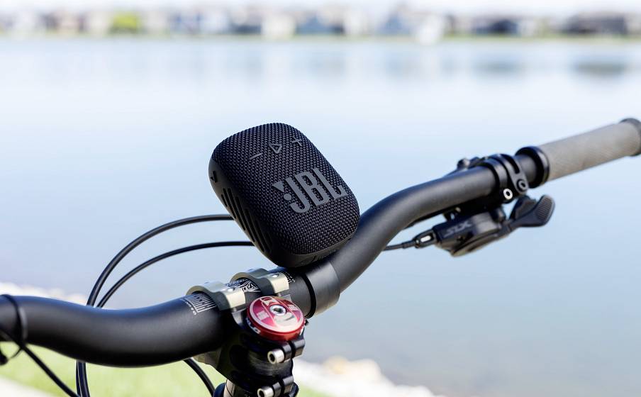 In the picture, the handlebars of a bicycle are visible by a lake, with a portable speaker mounted on them.