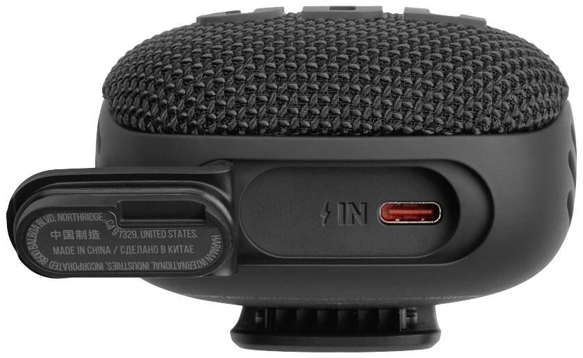 A portable speaker made of black fabric and plastic, showing a red USB-C port and an open flap with a label.
