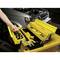 A person removes a screwdriver from a yellow toolbox on a trolley in front of a car with an open bonnet.