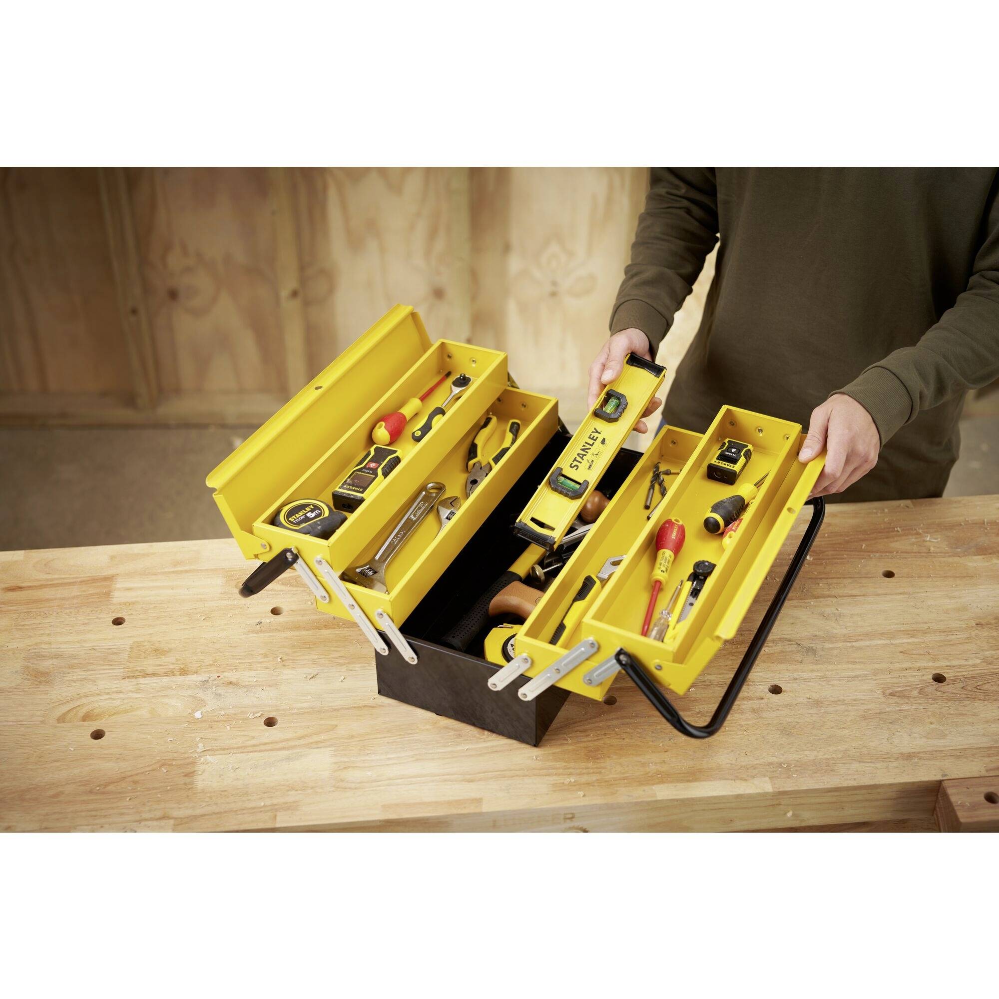 A person opens a yellow toolbox containing various tools such as pliers, screwdrivers and a spirit level.