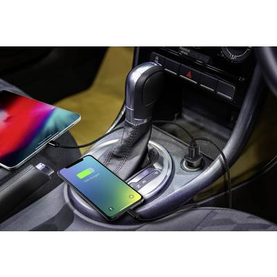 A smartphone and a tablet are connected and charging in the car; the smartphone's display shows '100% charged'.