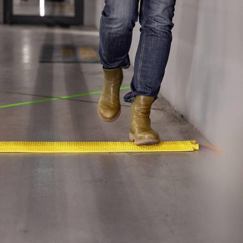 A person is walking on a pavement over a yellow, tactile strip that serves as a ground marking.
