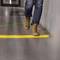A person is walking on a pavement over a yellow, tactile strip that serves as a ground marking.