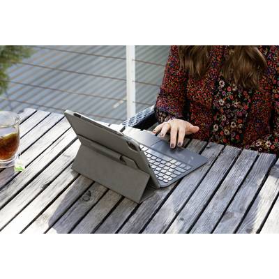 A person is sitting at a wooden table outdoors with a tablet and keyboard, alongside a glass of iced tea.