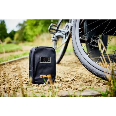 A black bag with an 'OSRAM' print sits on a sandy path next to a bicycle tyre, with trees visible in the background.