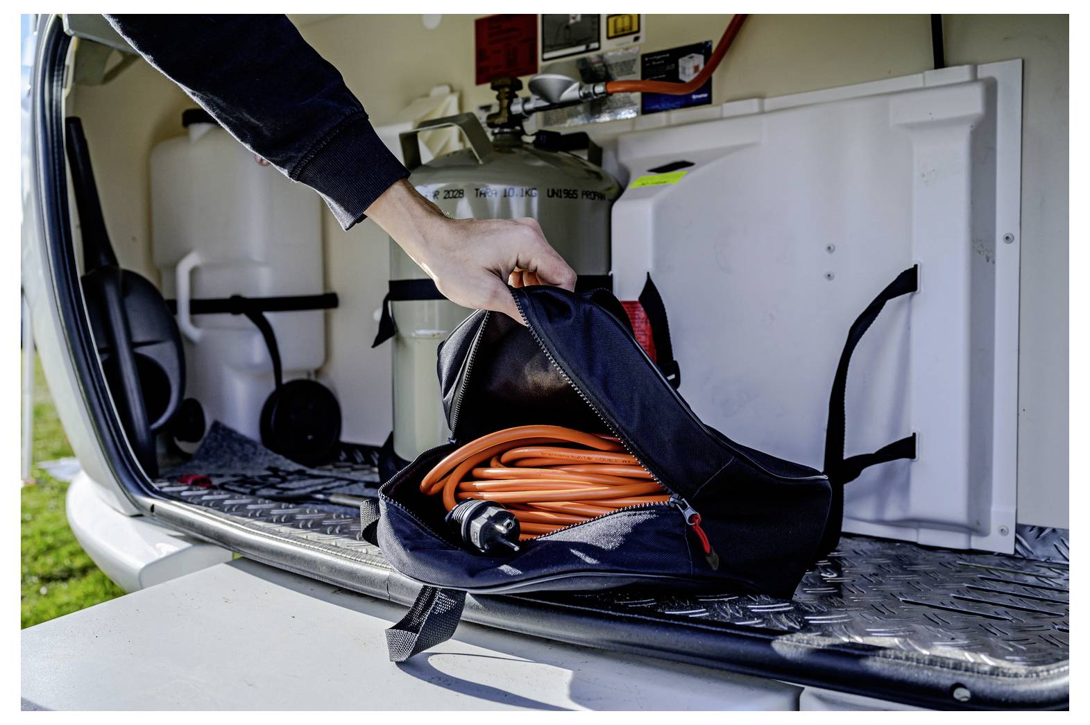Hand placing a black tool bag with orange cord in the back of a utility van.<br>