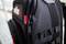 A black rucksack with a zip is shown in close-up, featuring a red logo on the left side.