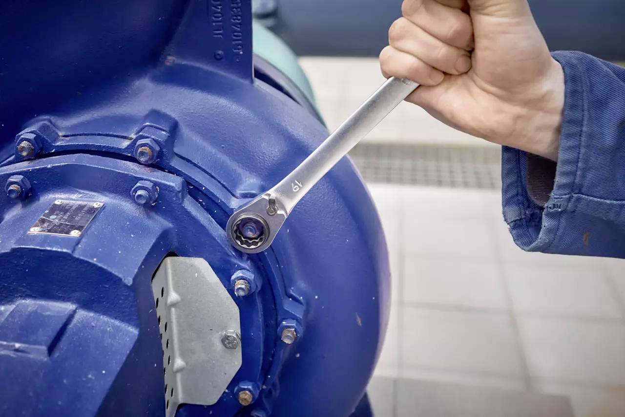 A person tightens a screw on a large blue machine valve with a spanner.