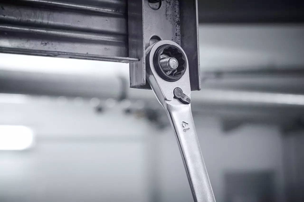A silver ratchet tightens a screw in a metal frame. The surroundings are blurred, focused on the tool.