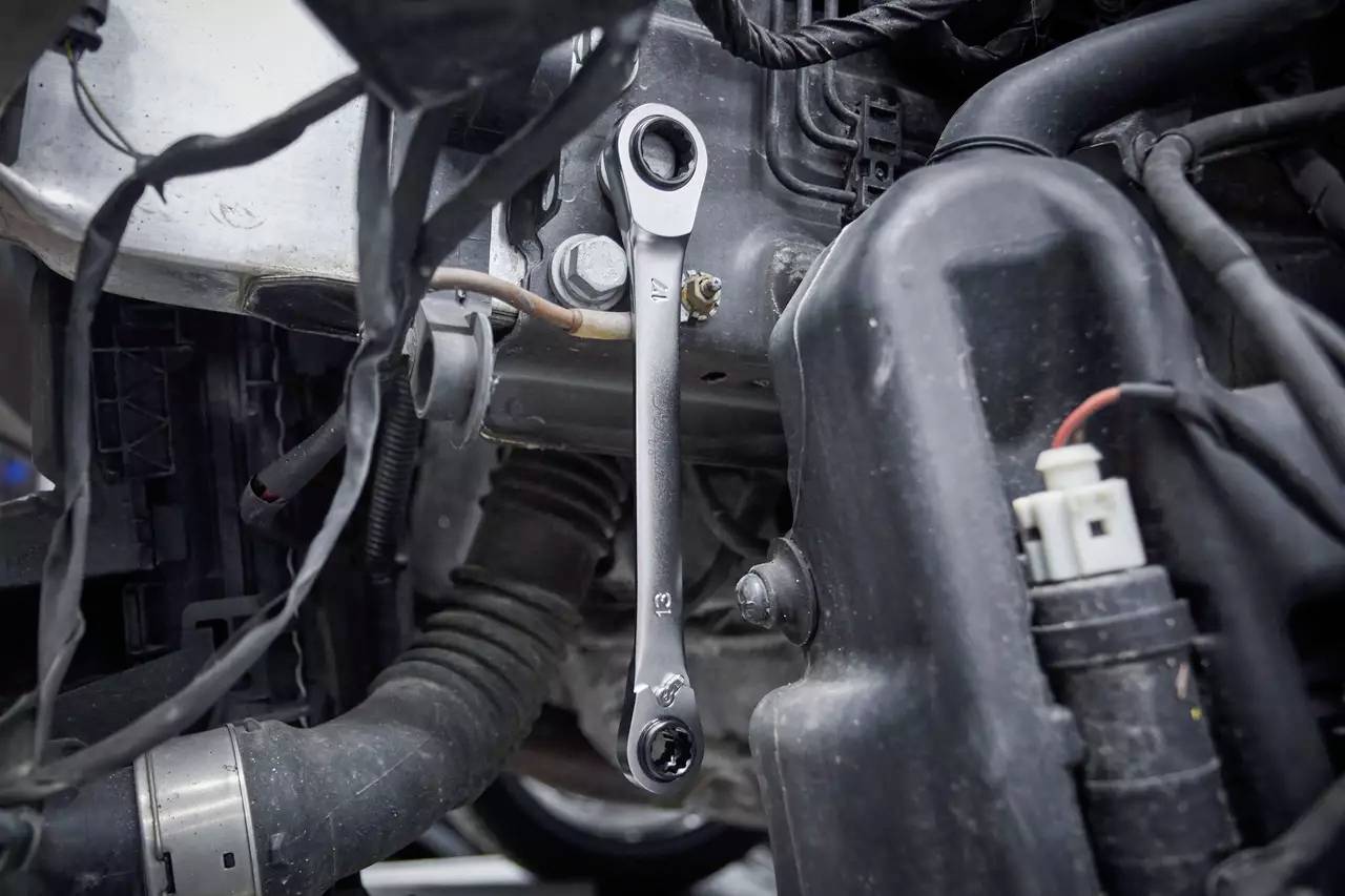A spanner is attached to a bolt in an engine compartment, surrounded by cables and other engine components.